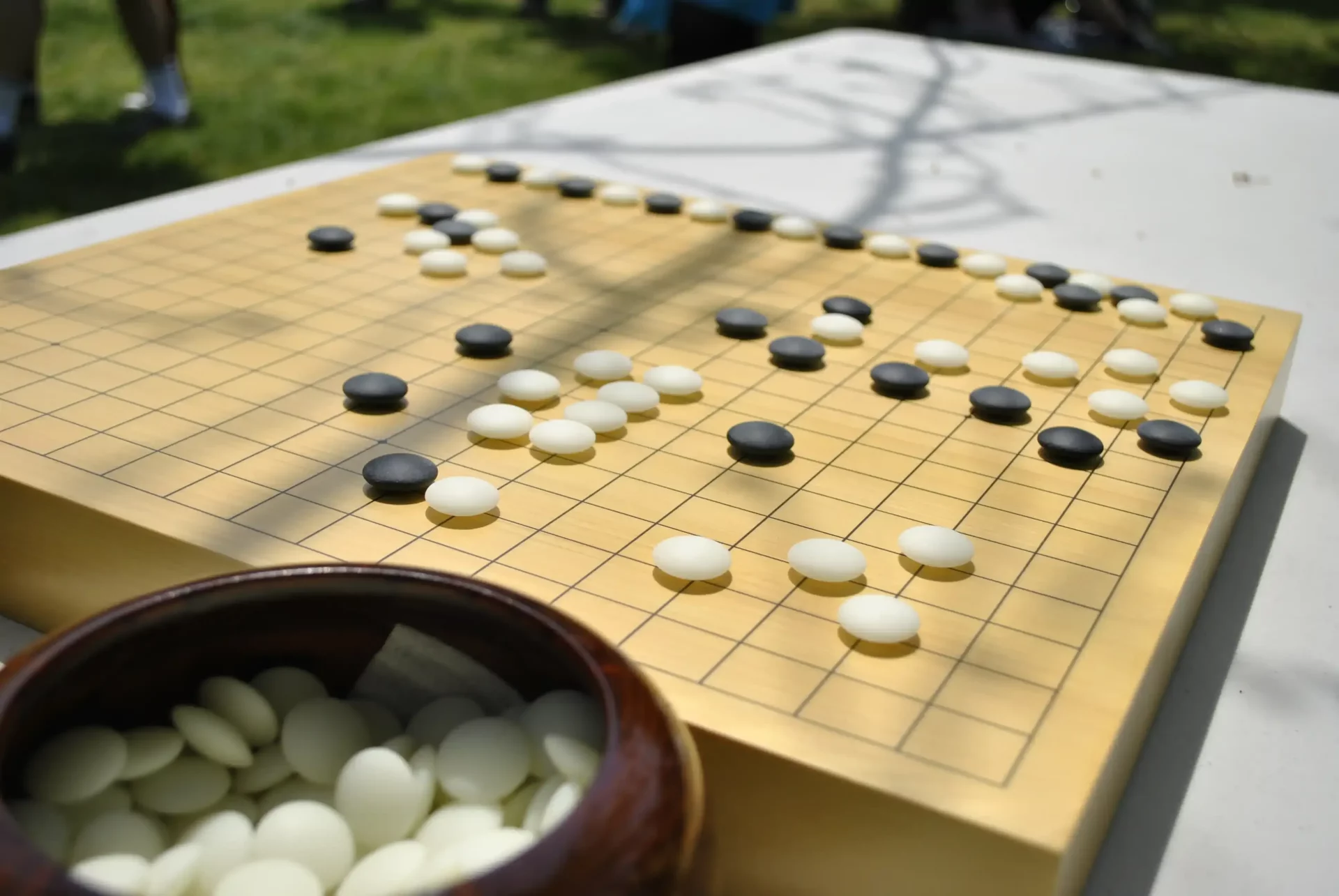 Tablero de Go con piezas blancas y negras en juego al aire libre, representando la estrategia del juego de mesa.